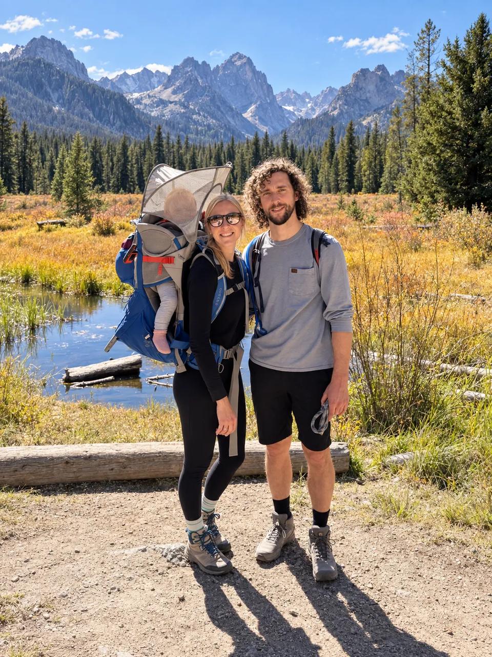 Audrey and Connor McCollough on a mountain trail with their baby in a hiking carrier, granite peaks and a fall meadow behind them